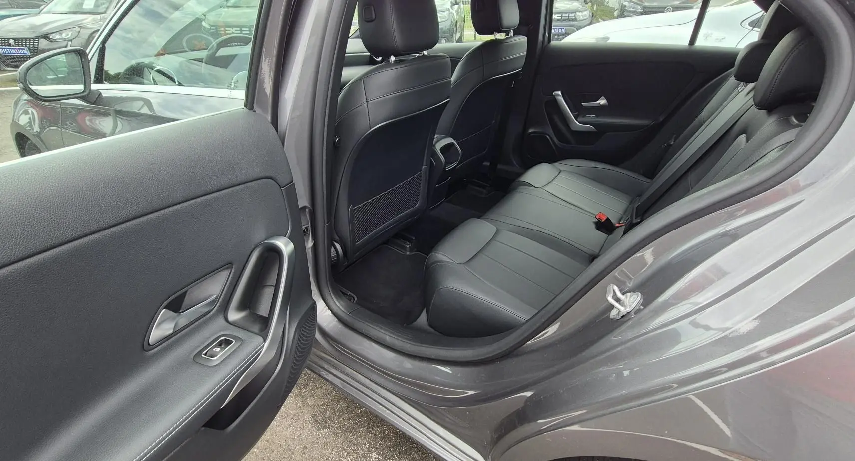 Vue côté gauche arrière montrant l’intérieur cuir noir et la porte ouverte d’une Mercedes Classe A 180d gris foncé 2020.
