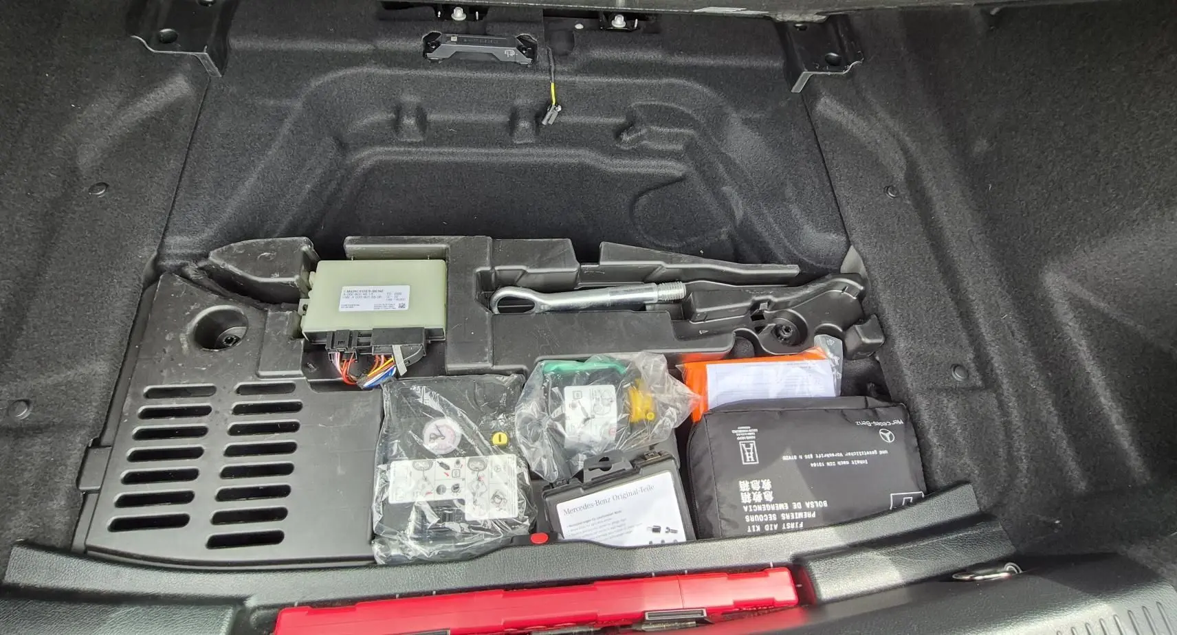 Coffre ouvert d’une Mercedes Classe A 180d gris foncé, montrant le kit anticrevaison et les outils de bord rangés sous le plancher.