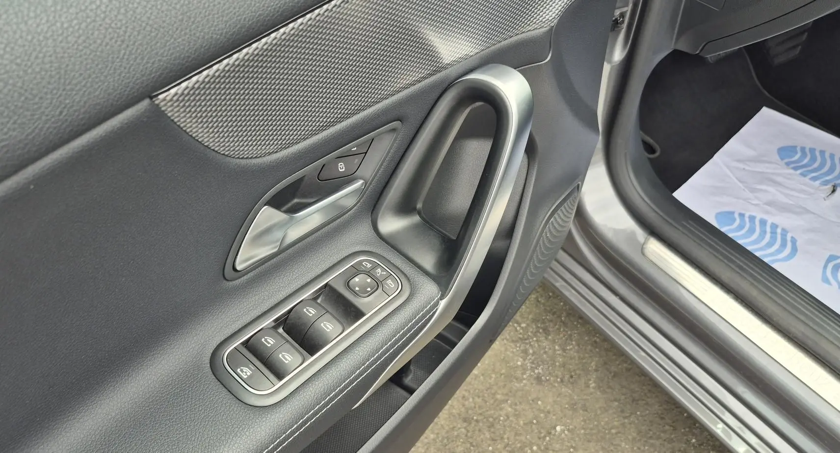 Gros plan sur la porte avant gauche gris foncé d'une Mercedes Classe A 180d 2020, avec commandes électriques et poignée argentée.