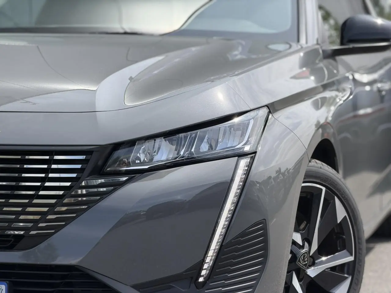 Gros plan sur l'avant droit gris Selenium du Peugeot 308 SW 2025, mettant en valeur le phare LED et la jante alliage 17 pouces.