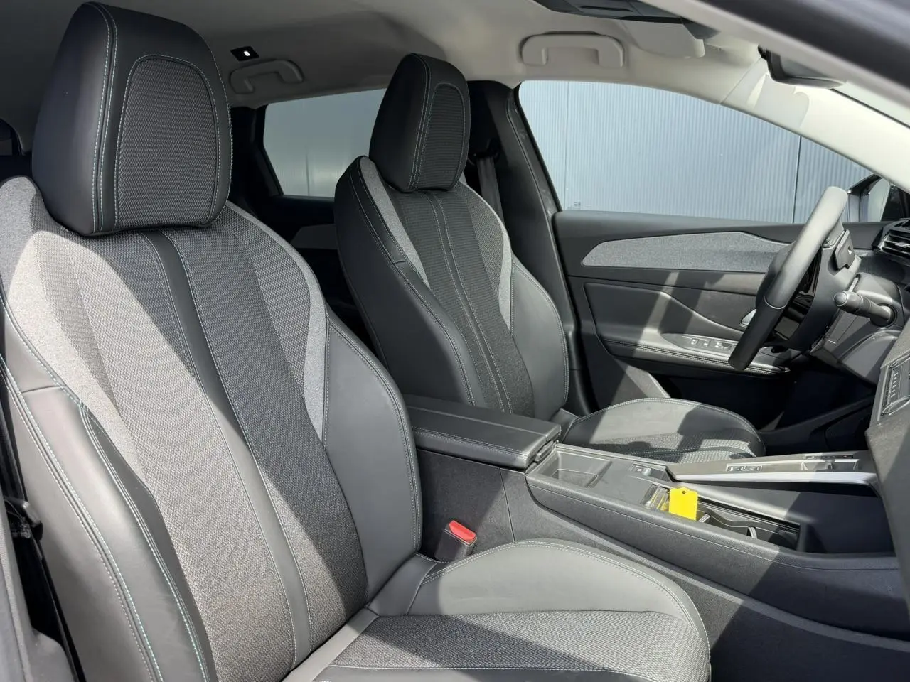 Vue intérieure côté droit du Peugeot 308 SW 2025, montrant les sièges bi-matière gris avec surpiqûres bleues et accoudoir central.