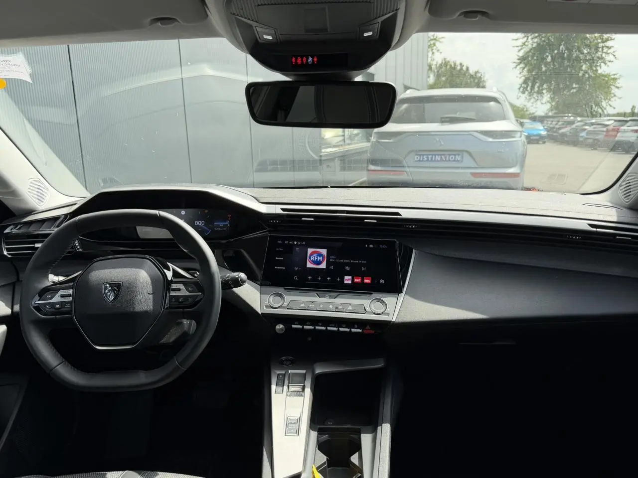 Vue intérieure frontale du poste de conduite de la Peugeot 308 SW 2025, avec tableau de bord noir et écran tactile central.