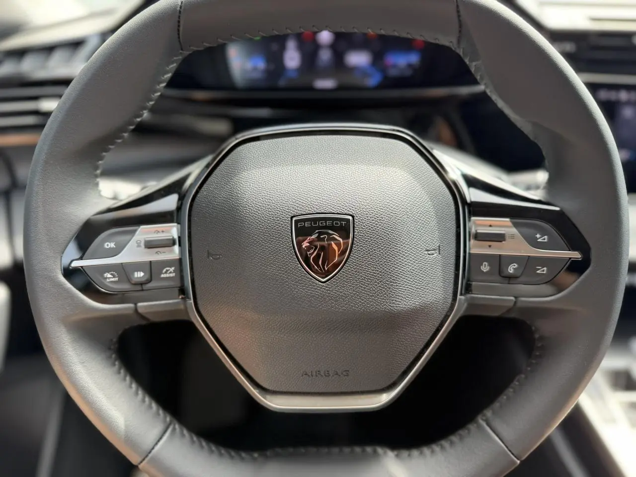 Gros plan sur le volant cuir noir du Peugeot 308 SW 2025 avec logo lion et commandes intégrées.
