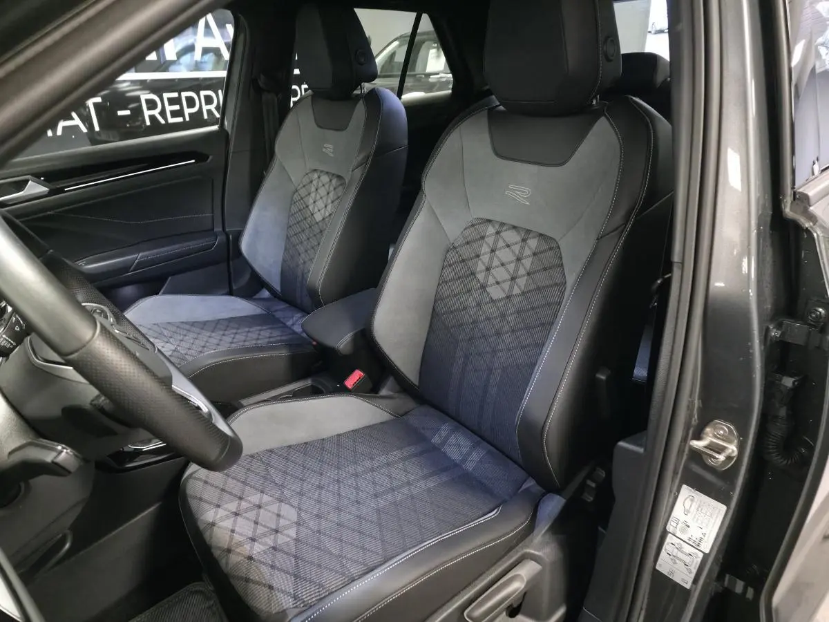 Vue intérieure côté gauche montrant les sièges avant gris avec surpiqûres et logo R-Line du Volkswagen T-Roc 2025.