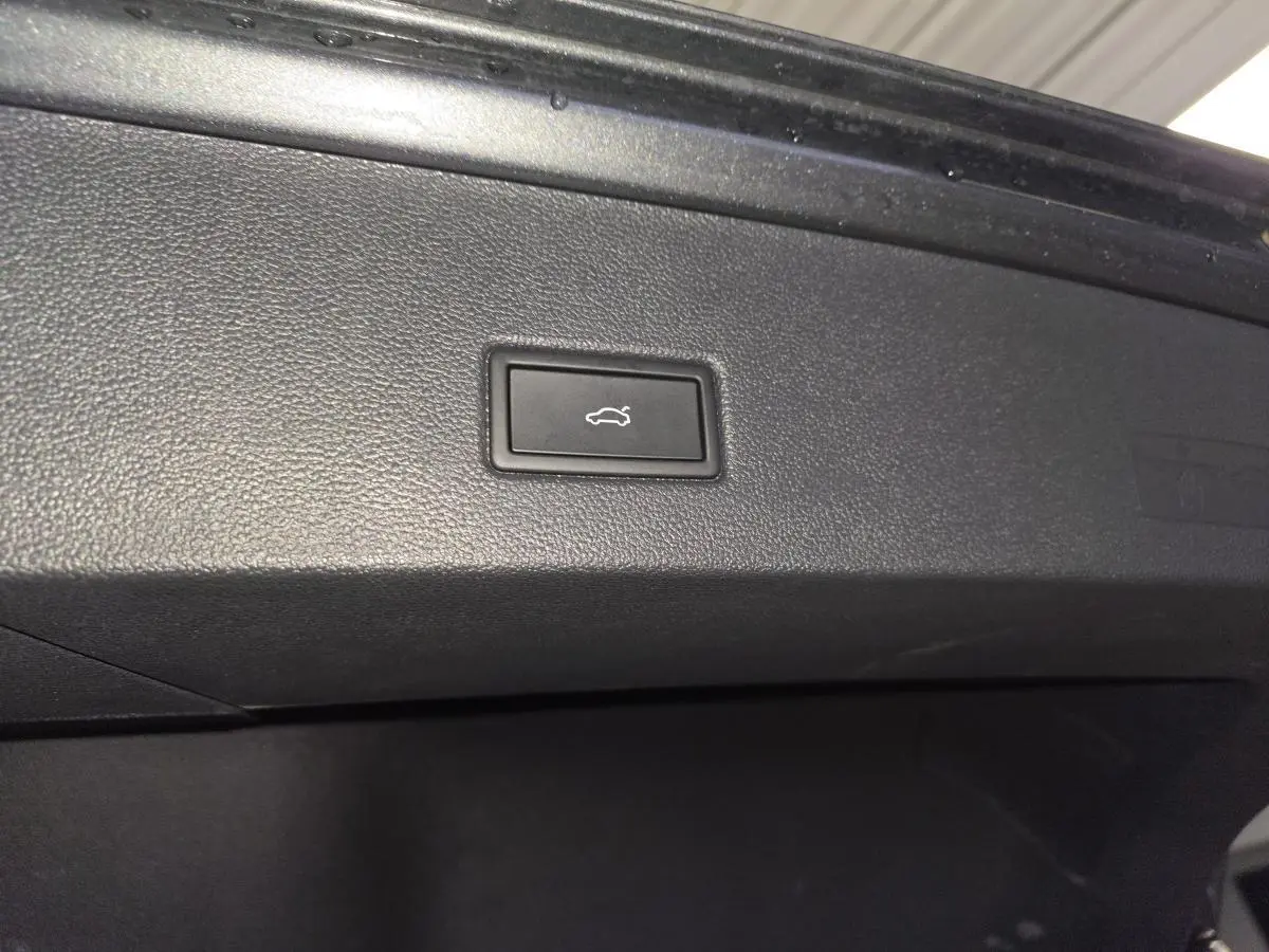 Gros plan sur le bouton d'ouverture électrique du hayon dans le coffre du Volkswagen T-Roc gris 2025 R-Line.