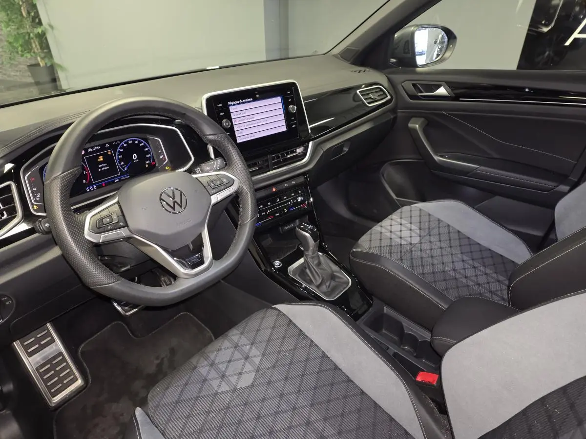 Intérieur avant du Volkswagen T-Roc 2025, vue côté conducteur, sièges gris et tableau de bord noir brillant.