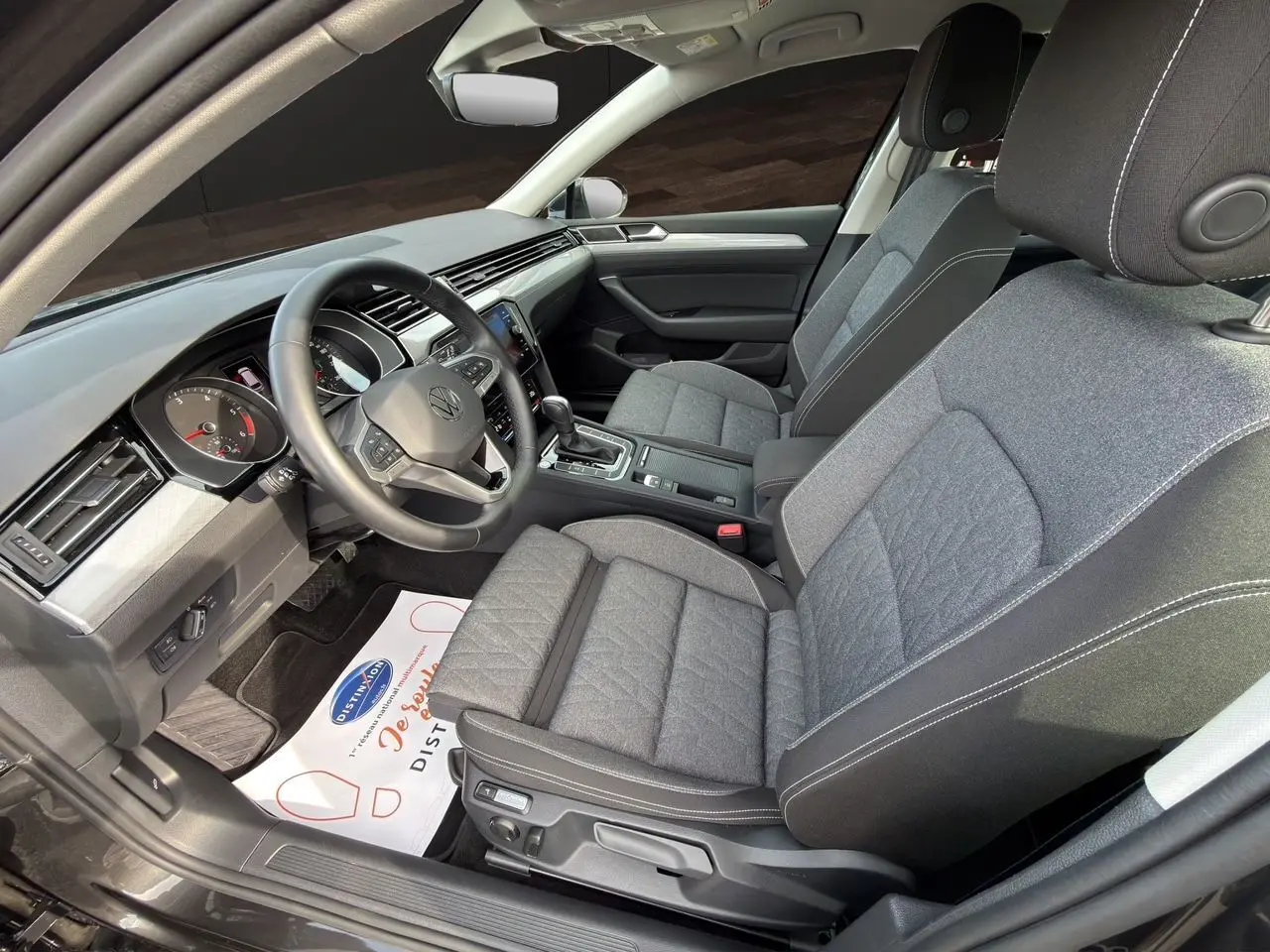 Vue intérieure côté conducteur de la Volkswagen Passat SW 2.0 TDI 2022 avec sièges tissu gris et volant multifonction cuir.