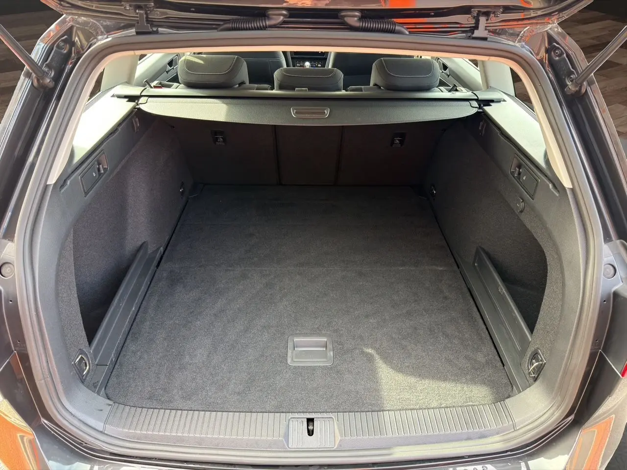 Coffre ouvert vu de l'arrière d'une Volkswagen Passat SW gris manganèse, espace de chargement vide et tapis noir.