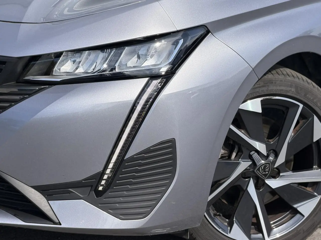 Gros plan sur l'avant droit gris Artense du Peugeot 308 SW 2025, mettant en valeur le phare LED et la jante alliage 17'' Halong.