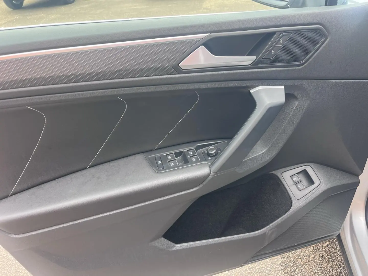 Vue intérieure côté gauche de la porte avant du Volkswagen Tiguan 2023 avec garniture noire et commandes électriques.