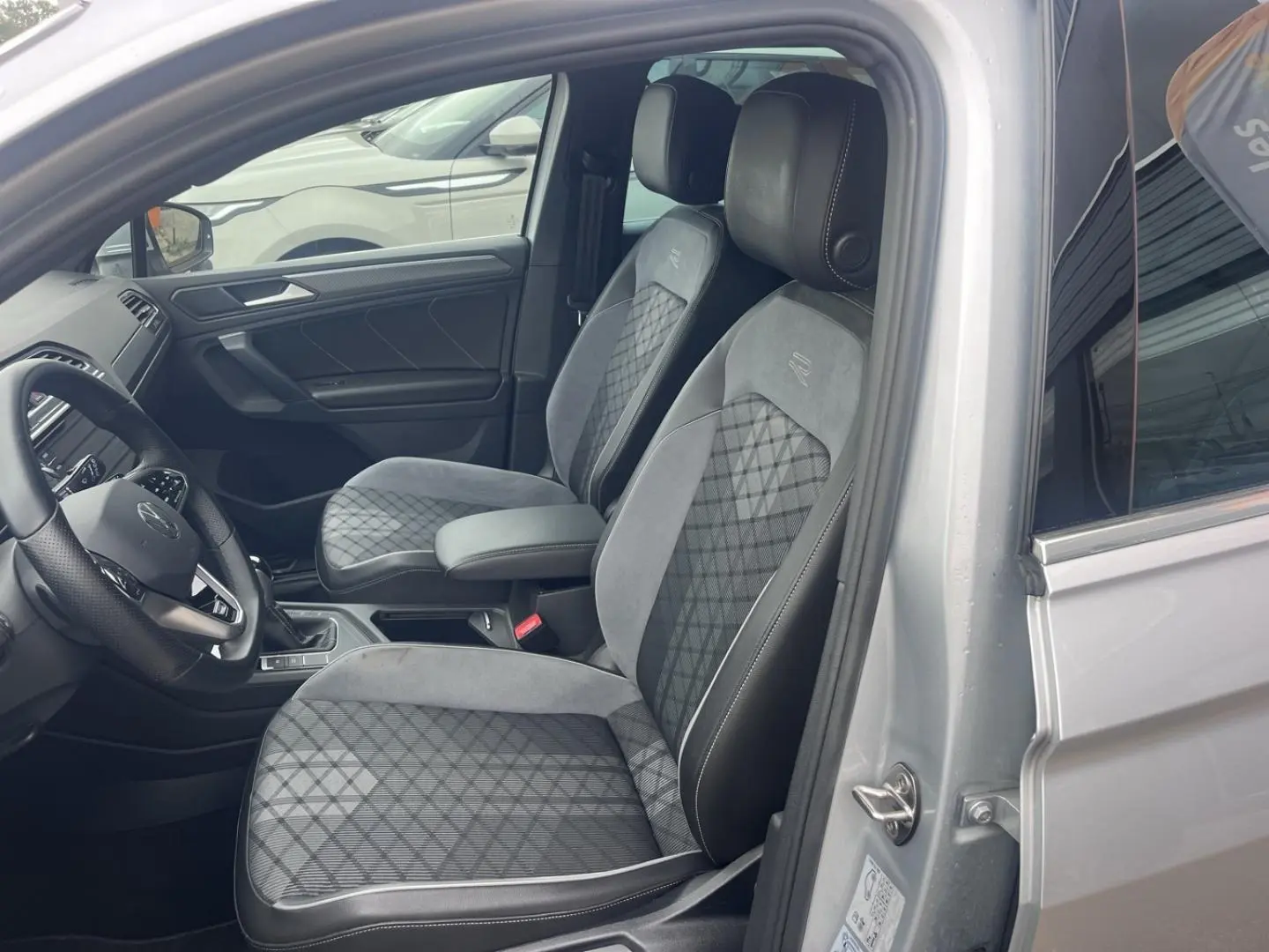 Vue intérieure côté conducteur du Volkswagen Tiguan gris dauphin, sièges sport R-Line avec surpiqûres contrastées.