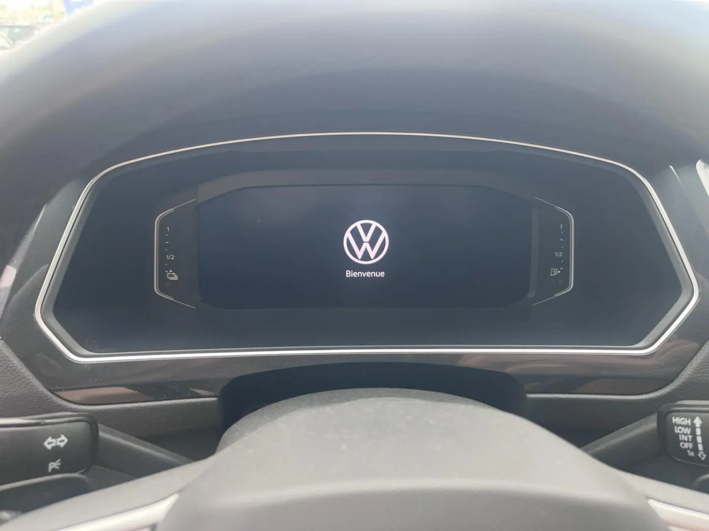 Vue rapprochée du tableau de bord numérique noir du Volkswagen Tiguan 1.4 eHybrid 2023 affichant le logo VW et "Bienvenue".