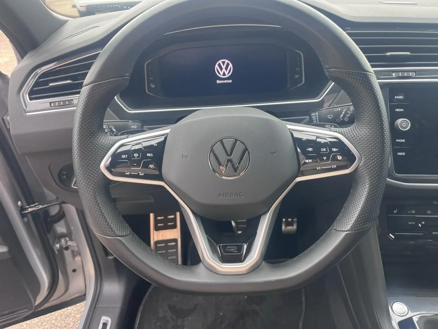 Vue rapprochée du volant cuir multifonction noir du Volkswagen Tiguan 2023 avec écran digital en arrière-plan.