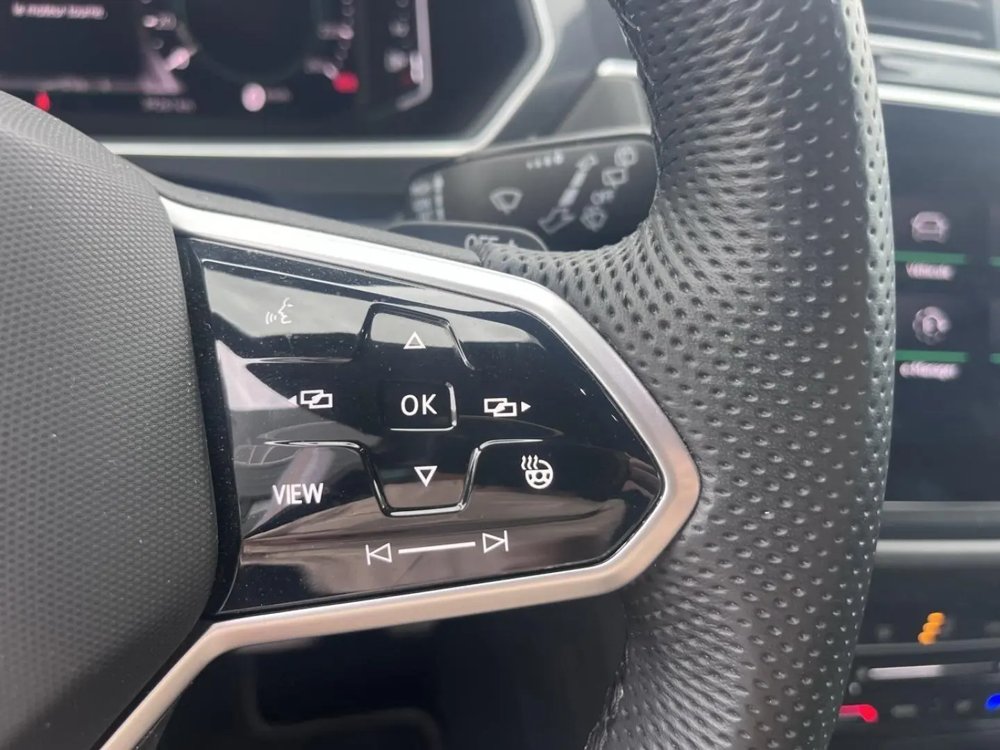 Gros plan sur les commandes multifonctions noires à gauche du volant cuir perforé du Volkswagen Tiguan gris Dauphin.