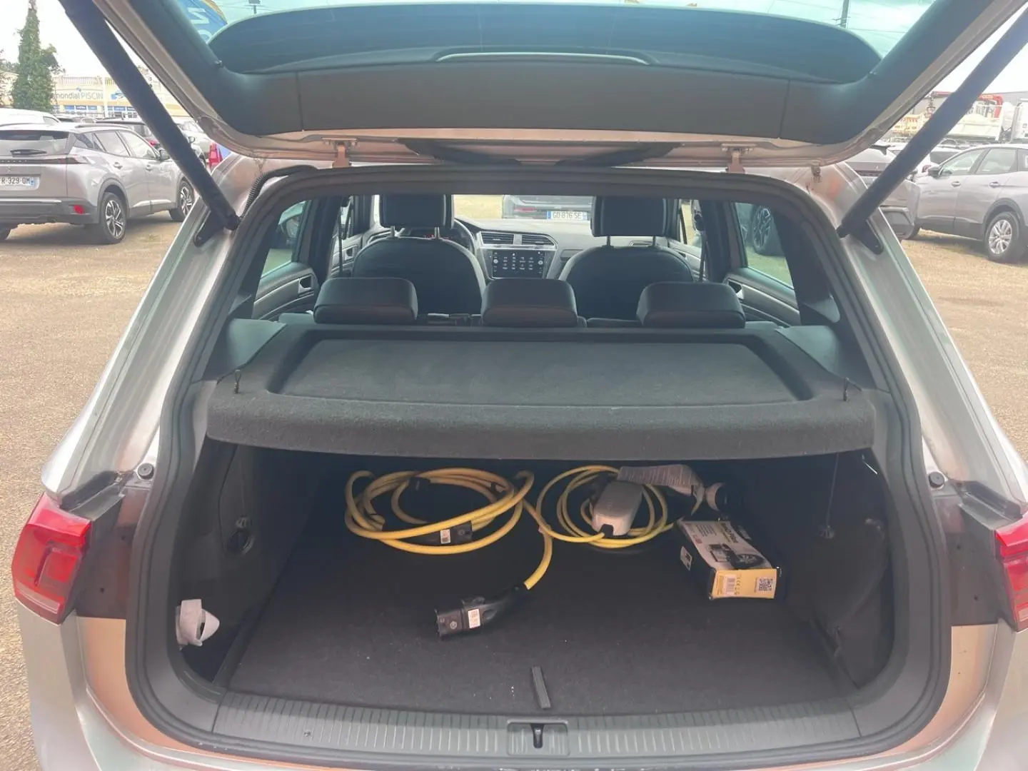 Coffre ouvert d’un Volkswagen Tiguan gris dauphin 2023, vue arrière montrant câbles de recharge hybride et intérieur noir.