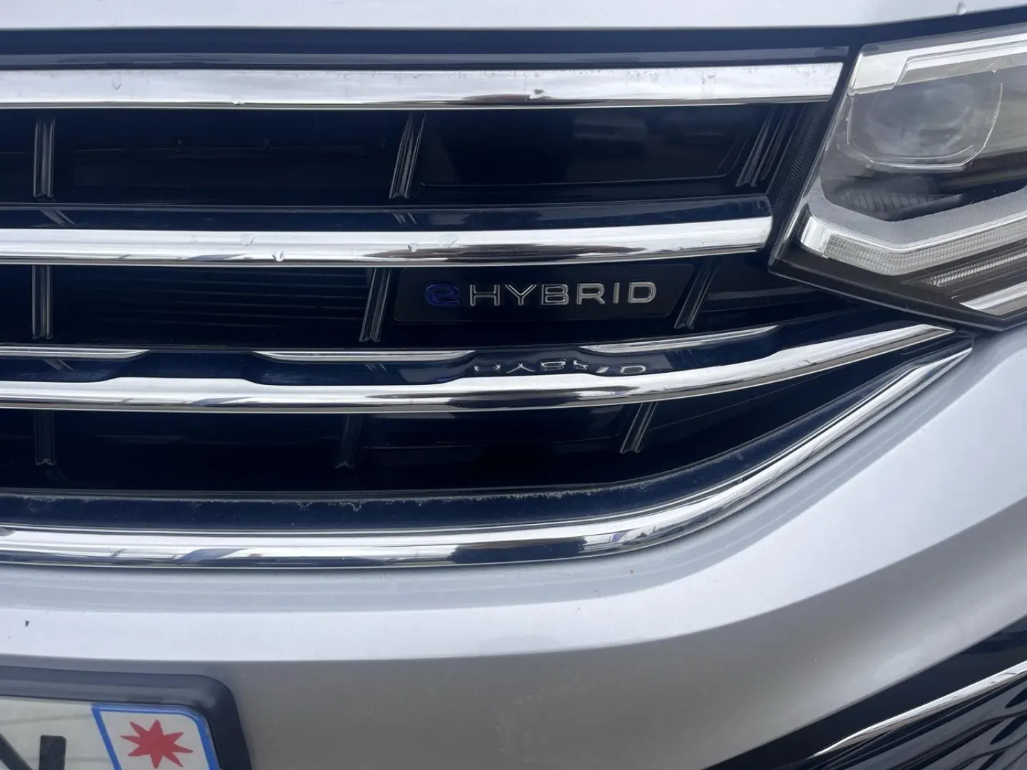 Gros plan sur la calandre avant gris dauphin métallisée du Volkswagen Tiguan 1.4 eHybrid avec badge eHybrid visible.