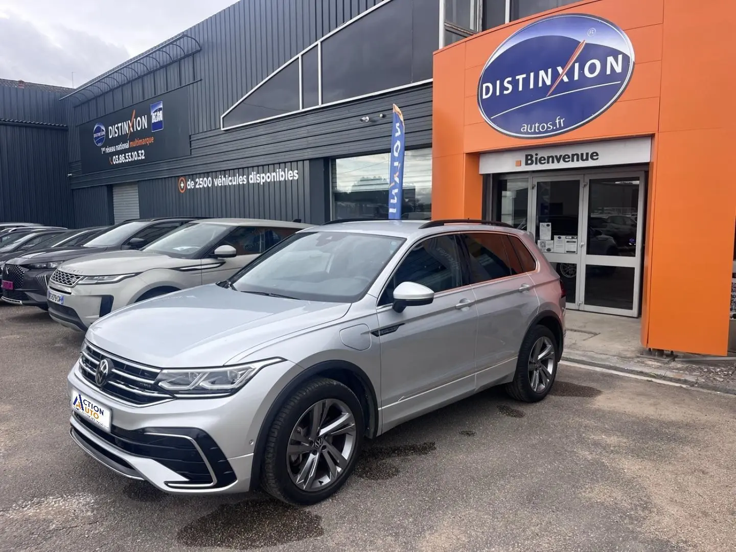 Vue 3/4 avant droit du Volkswagen Tiguan gris dauphin métallisé avec jantes alliage et toit noir devant un concessionnaire.