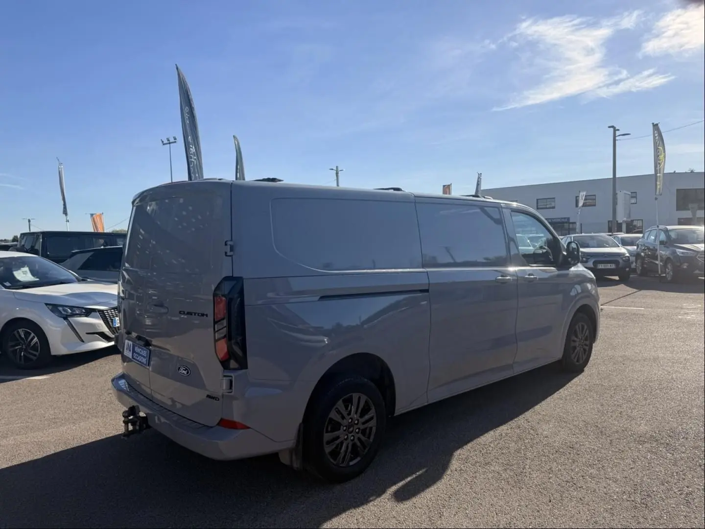 Vue 3/4 arrière droite du Ford Transit Custom Fourgon gris 2024 avec attelage et jantes foncées.