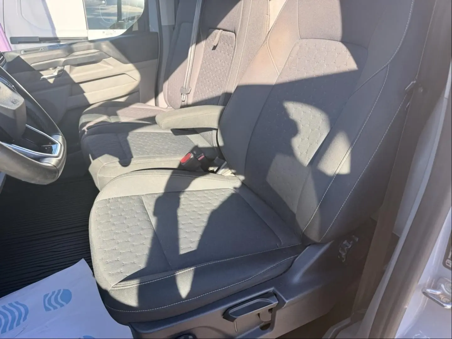 Vue intérieure côté conducteur du Ford Transit Custom Fourgon gris 2024, mettant en valeur les sièges en tissu et l'accoudoir central.