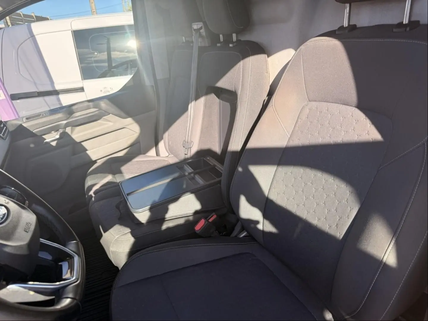 Vue intérieure côté conducteur du Ford Transit Custom Fourgon gris 2024, montrant les sièges avant et le volant.