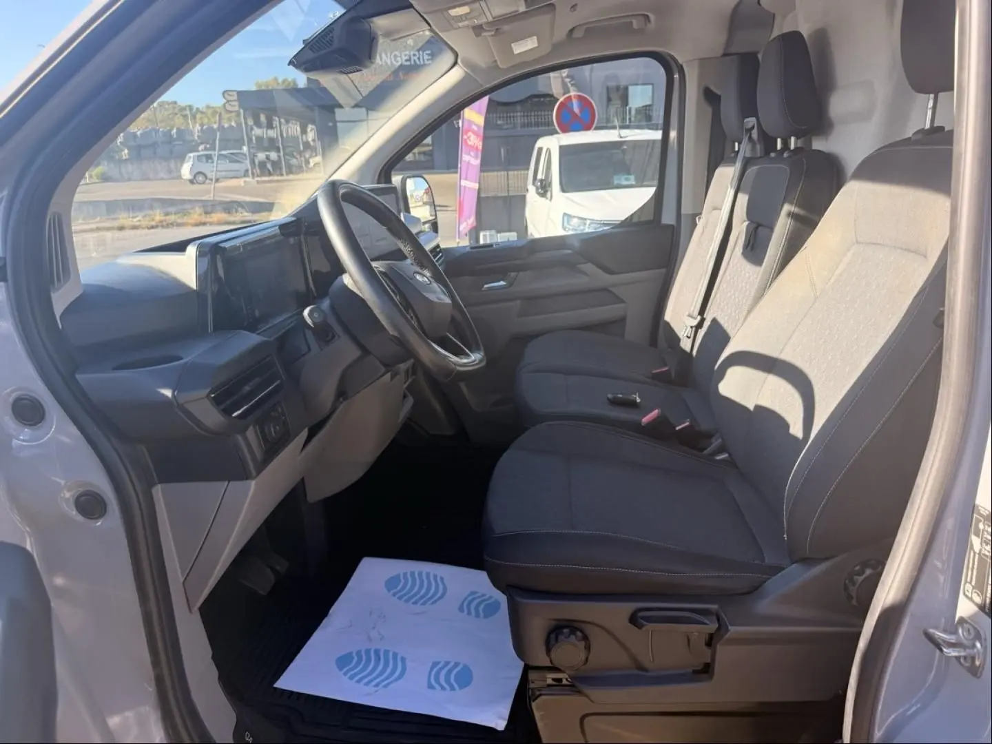 Vue intérieure côté conducteur du Ford Transit Custom Fourgon gris 2024, sièges tissu et tableau de bord moderne.