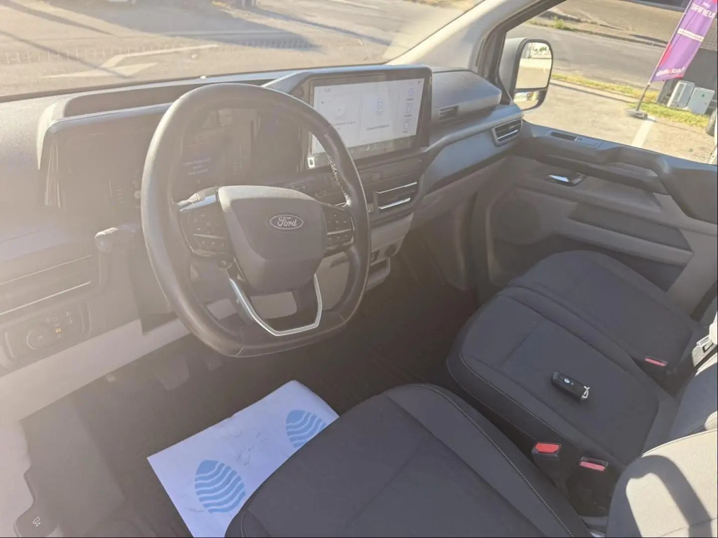 Vue intérieure côté conducteur du Ford Transit Custom Fourgon gris 2024, avec volant multifonction et écran tactile central.