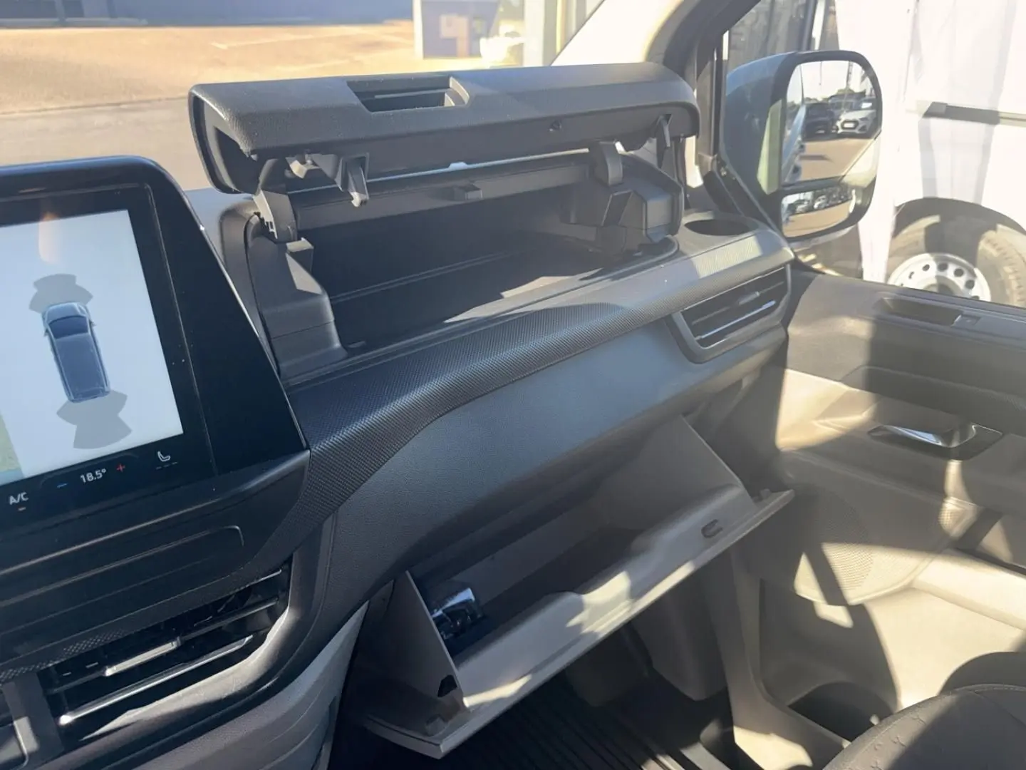 Intérieur du Ford Transit Custom 2024, vue côté passager montrant tableau de bord gris et rangements ouverts.
