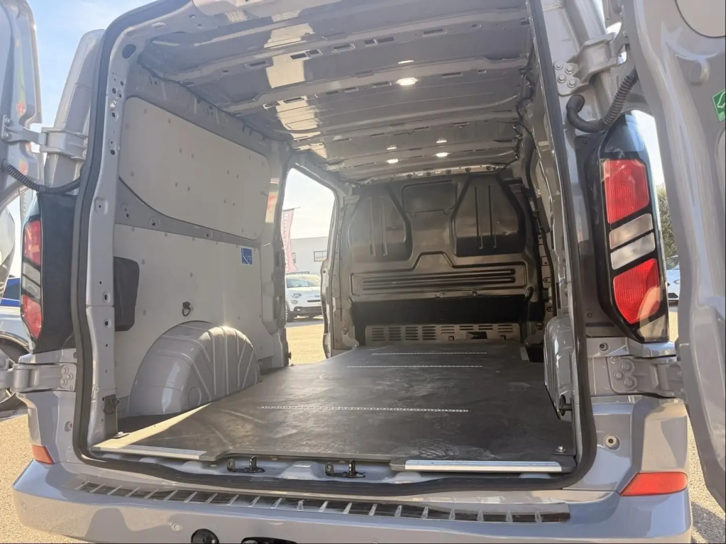 Vue arrière ouverte du Ford Transit Custom Fourgon gris 2024, montrant l'espace de chargement vide et le plancher plat.