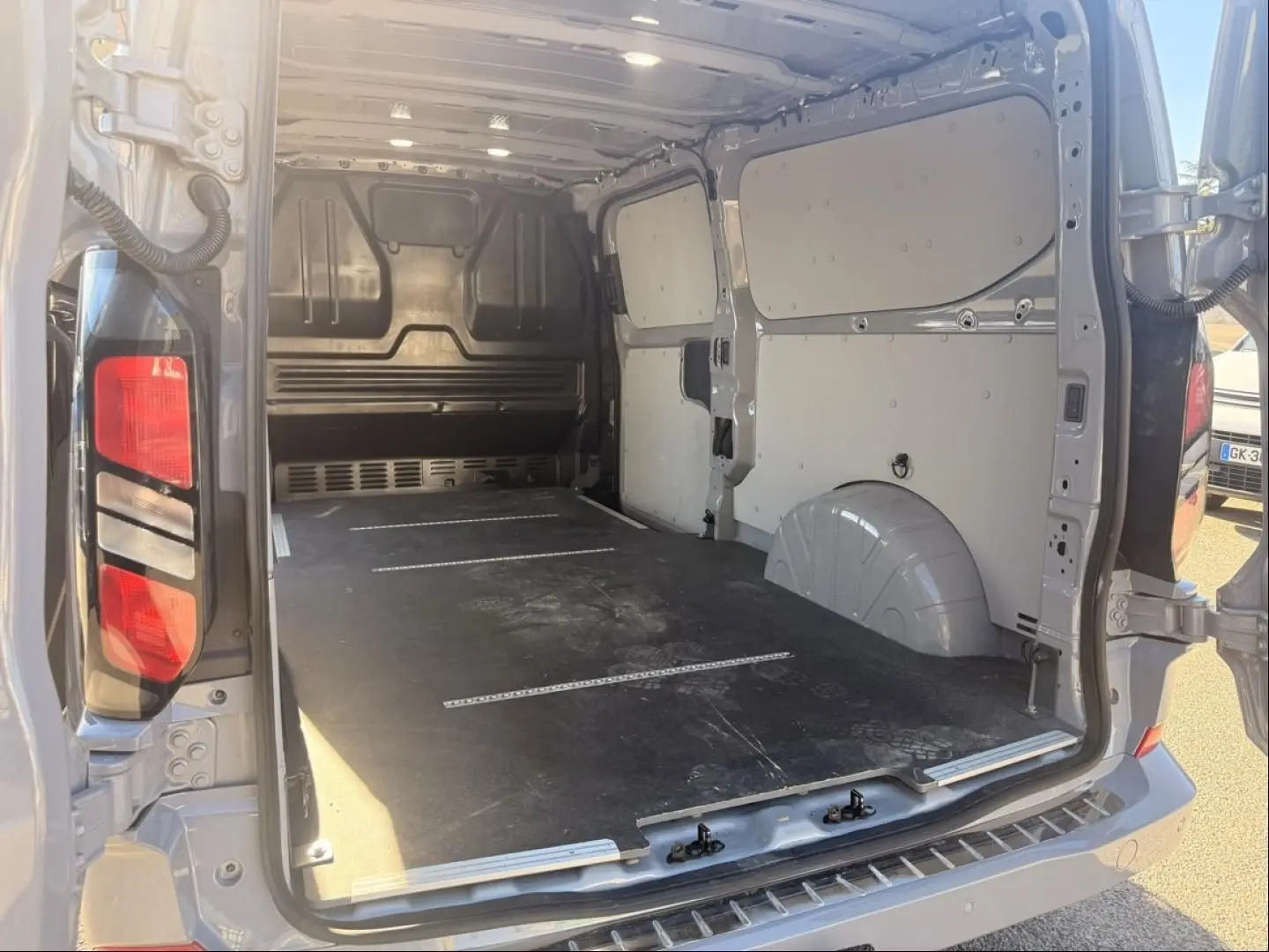 Vue arrière ouverte du Ford Transit Custom Fourgon gris 2024, montrant l’espace de chargement vide et les portes battantes.