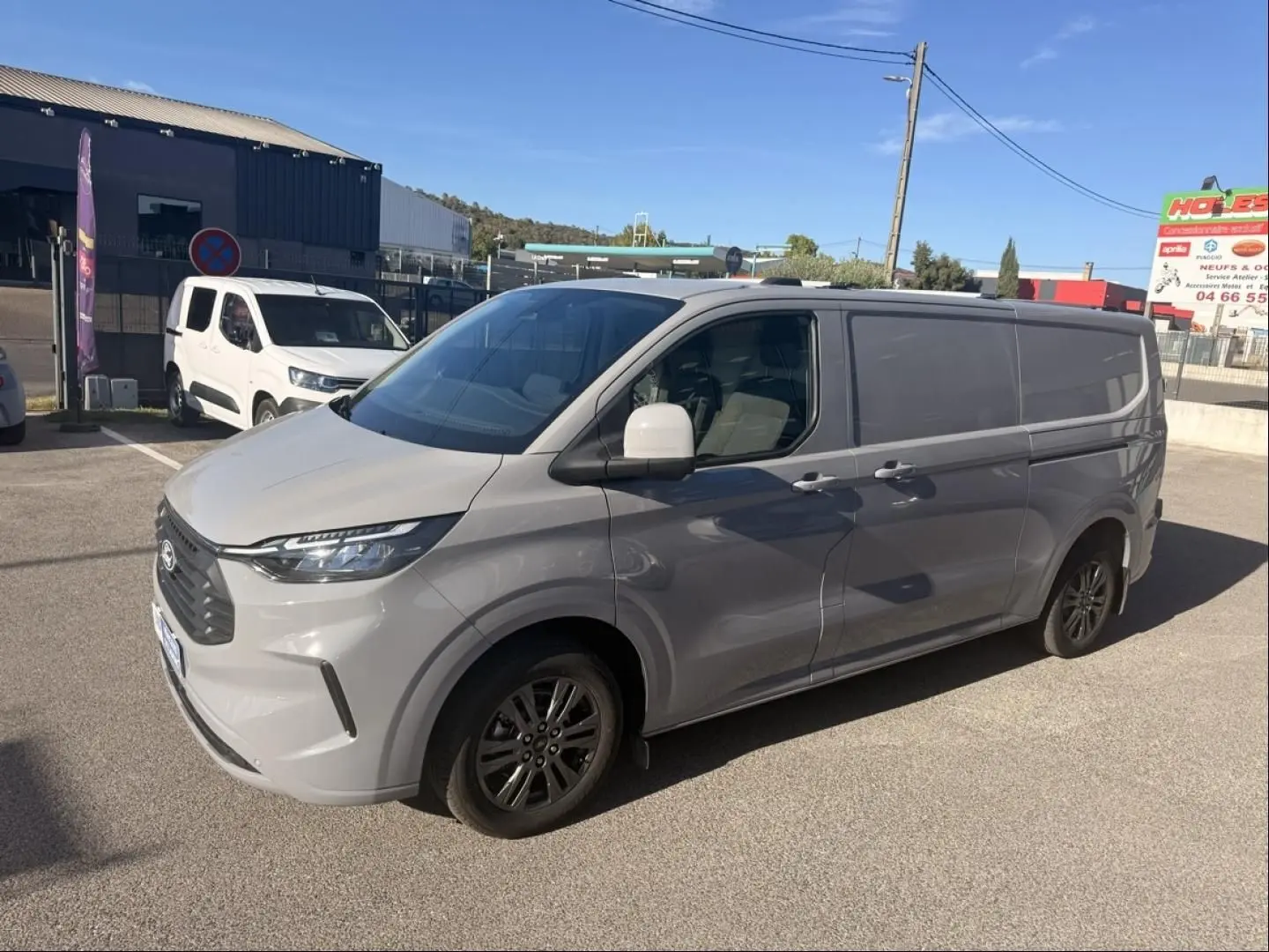 Ford Transit Custom Fourgon gris, vue 3/4 avant droit, avec jantes foncées et calandre marquée, stationné en extérieur.