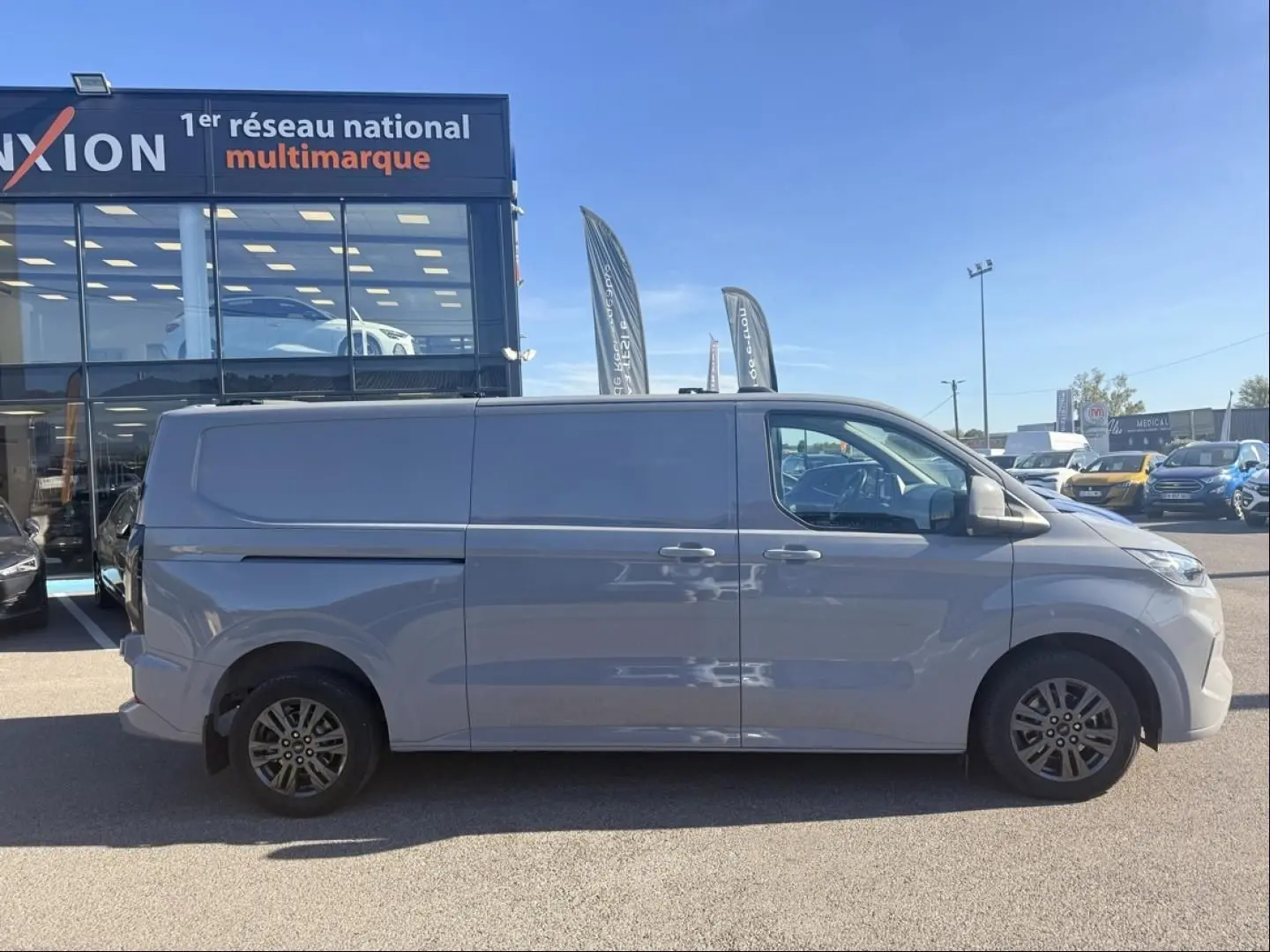 Vue de profil côté droit du Ford Transit Custom Fourgon gris 2024, finition Limited 4x4, stationné en extérieur.