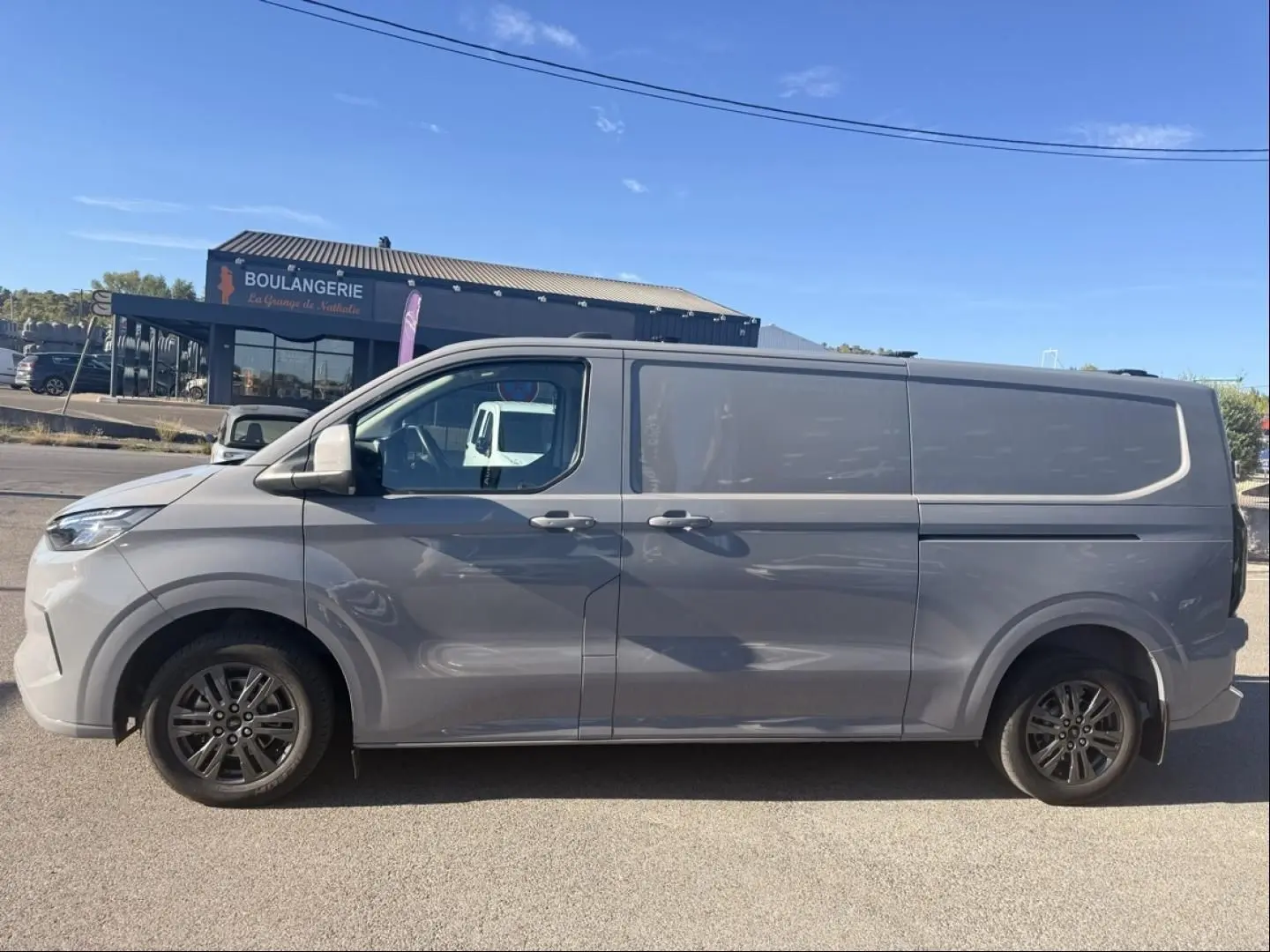 Vue latérale gauche d’un Ford Transit Custom Fourgon gris 2024 avec jantes alliage et carrosserie lisse.