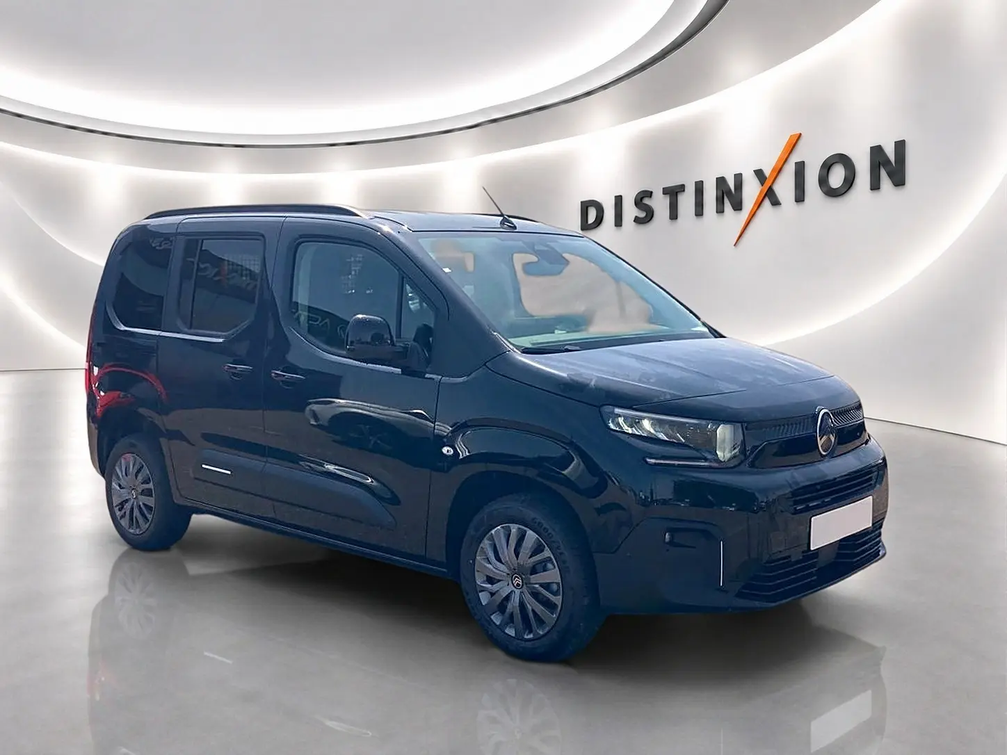 Vue 3/4 avant d’un Citroën Berlingo noir 2026 avec barres de toit et jantes alu dans un showroom lumineux.