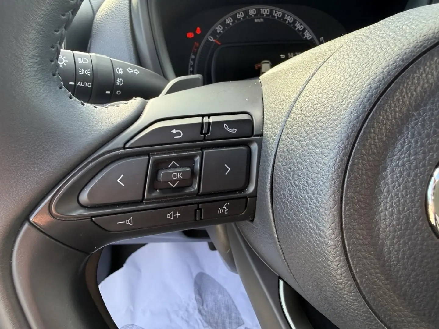 Gros plan sur les commandes au volant noir de la Toyota Aygo X 2025, avec tableau de bord partiellement visible.