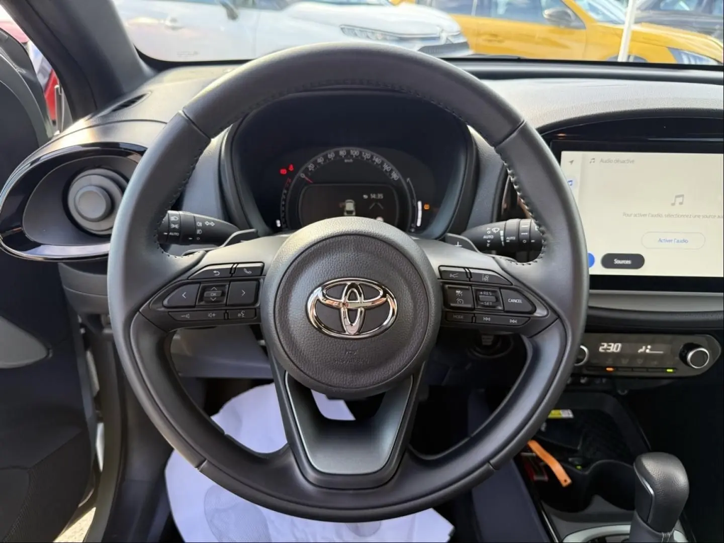 Vue intérieure centrée sur le volant noir de la Toyota Aygo X 2025 avec tableau de bord et écran tactile visibles.
