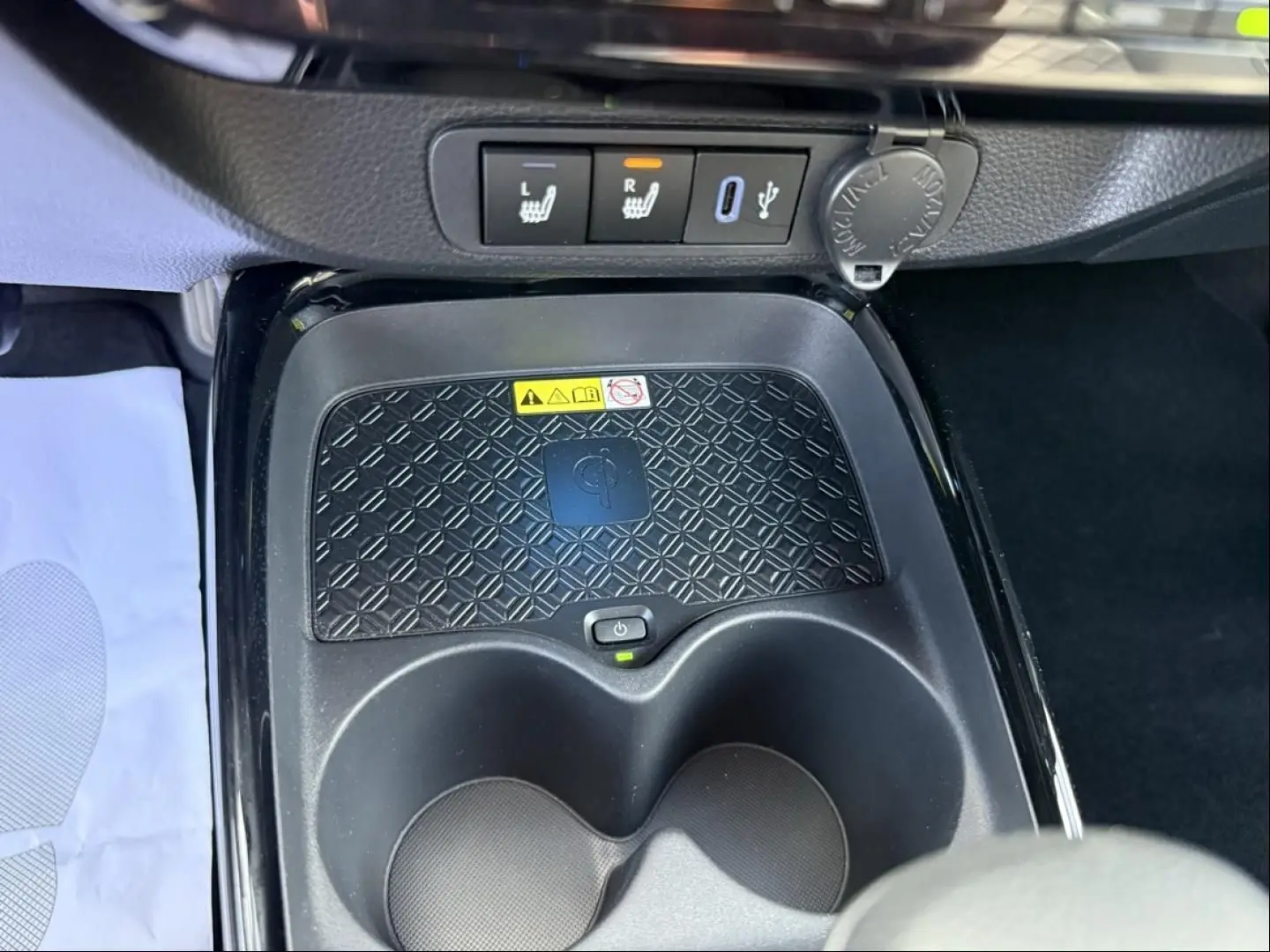 Gros plan sur la console centrale de la Toyota Aygo X 2025, montrant le chargeur sans fil, porte-gobelets et commandes de sièges chauffants.