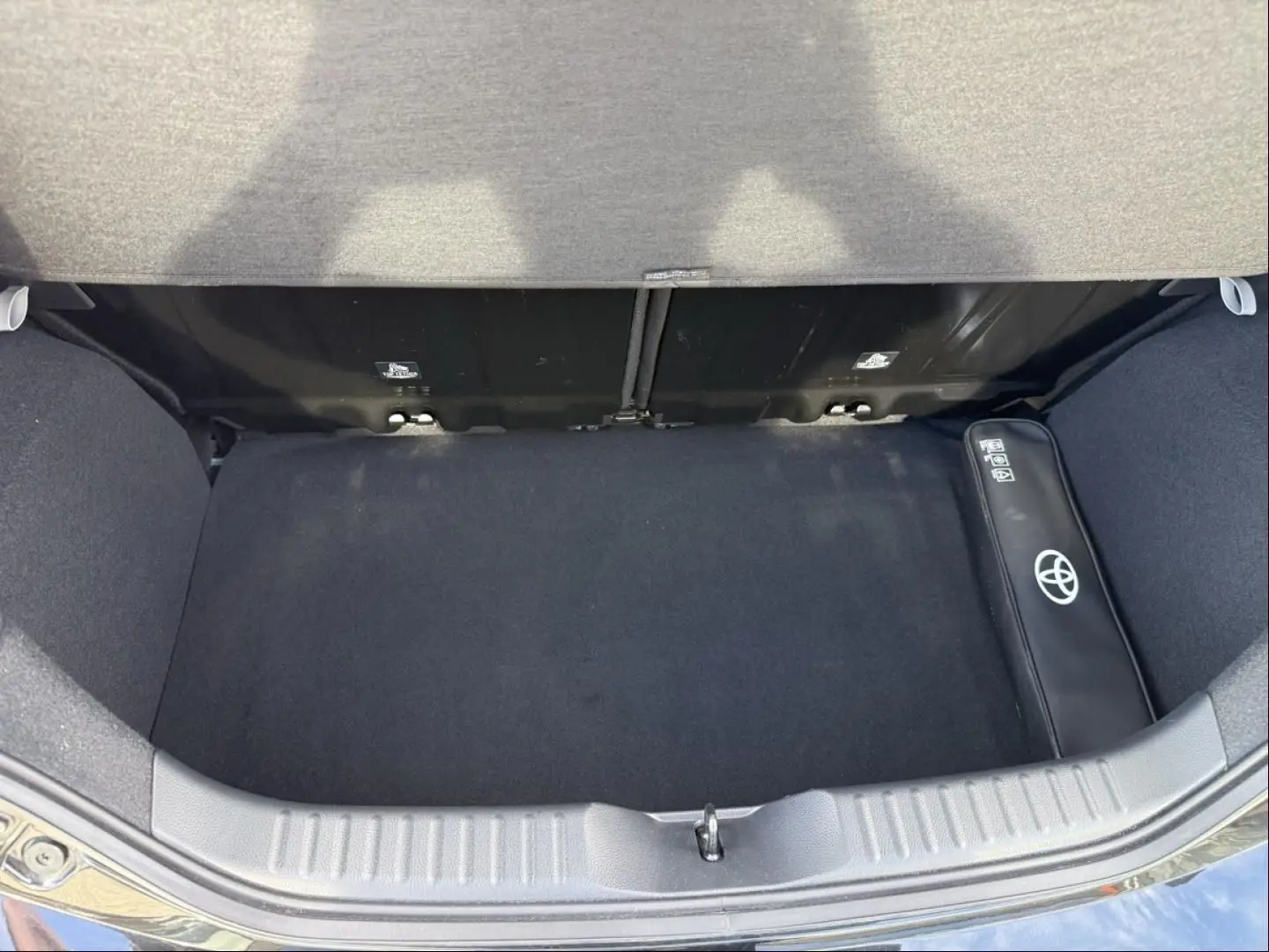Coffre ouvert vu de dessus d’une Toyota Aygo X 2025 vert aventurine avec toit noir, sac Toyota visible à droite.