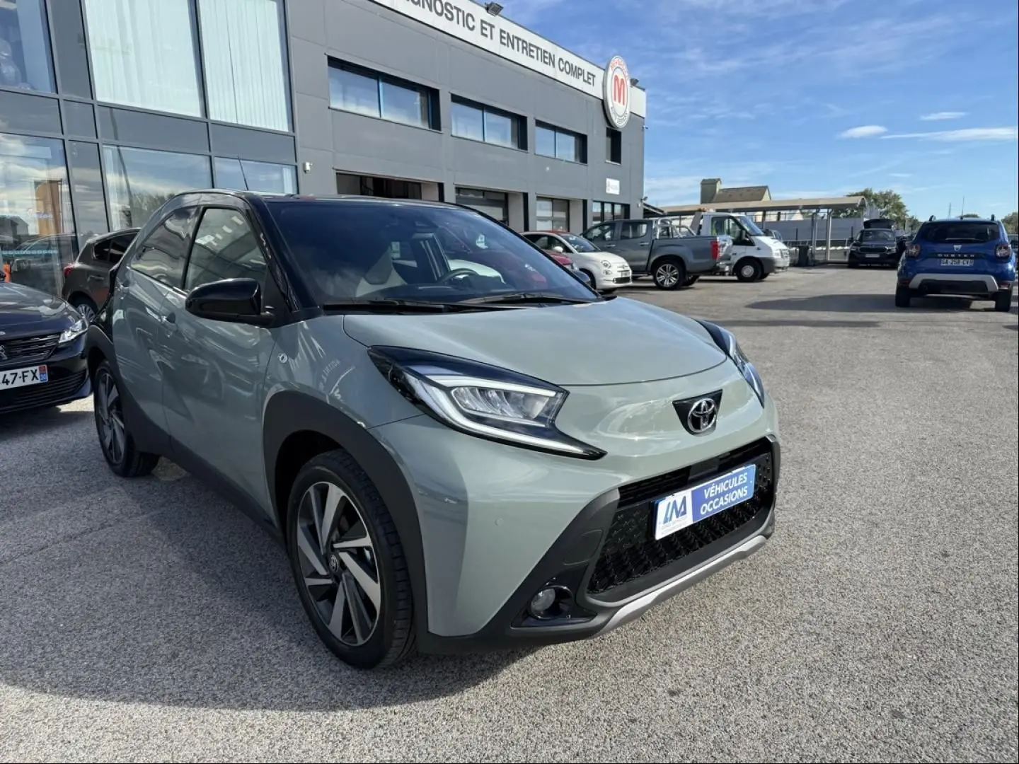 Toyota Aygo X vert aventurine avec toit noir, vue 3/4 avant droit, mettant en valeur ses phares anguleux et sa calandre noire.