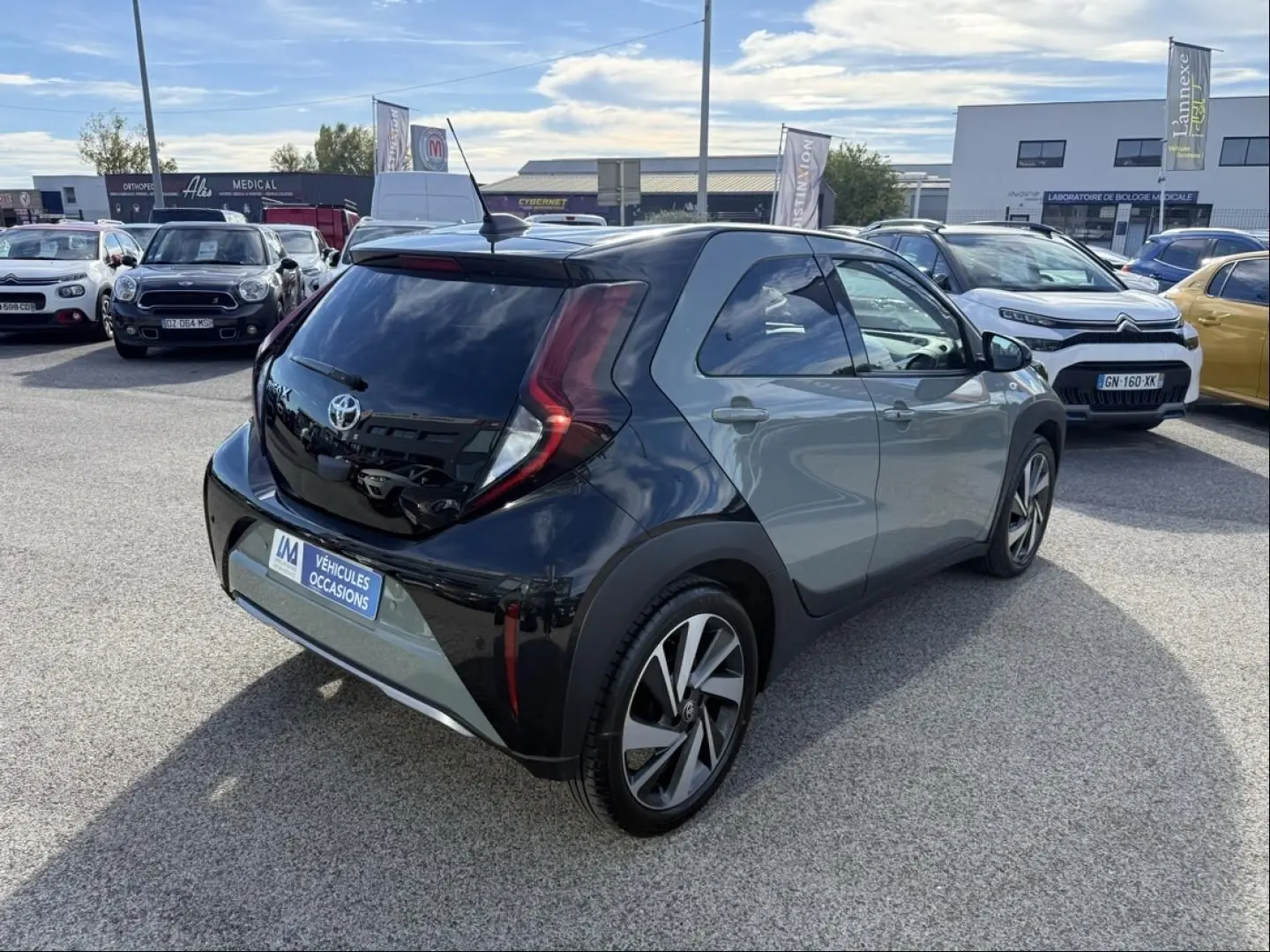 Toyota Aygo X 2025 en vert aventurine avec toit noir, vue 3/4 arrière droit, stationnée en extérieur sur parking.