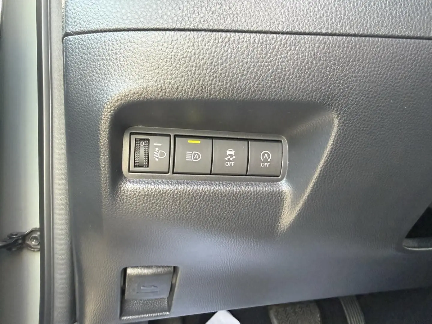 Gros plan sur les commandes de réglage des phares et d'assistance à la conduite dans une Toyota Aygo X 2025, intérieur noir.