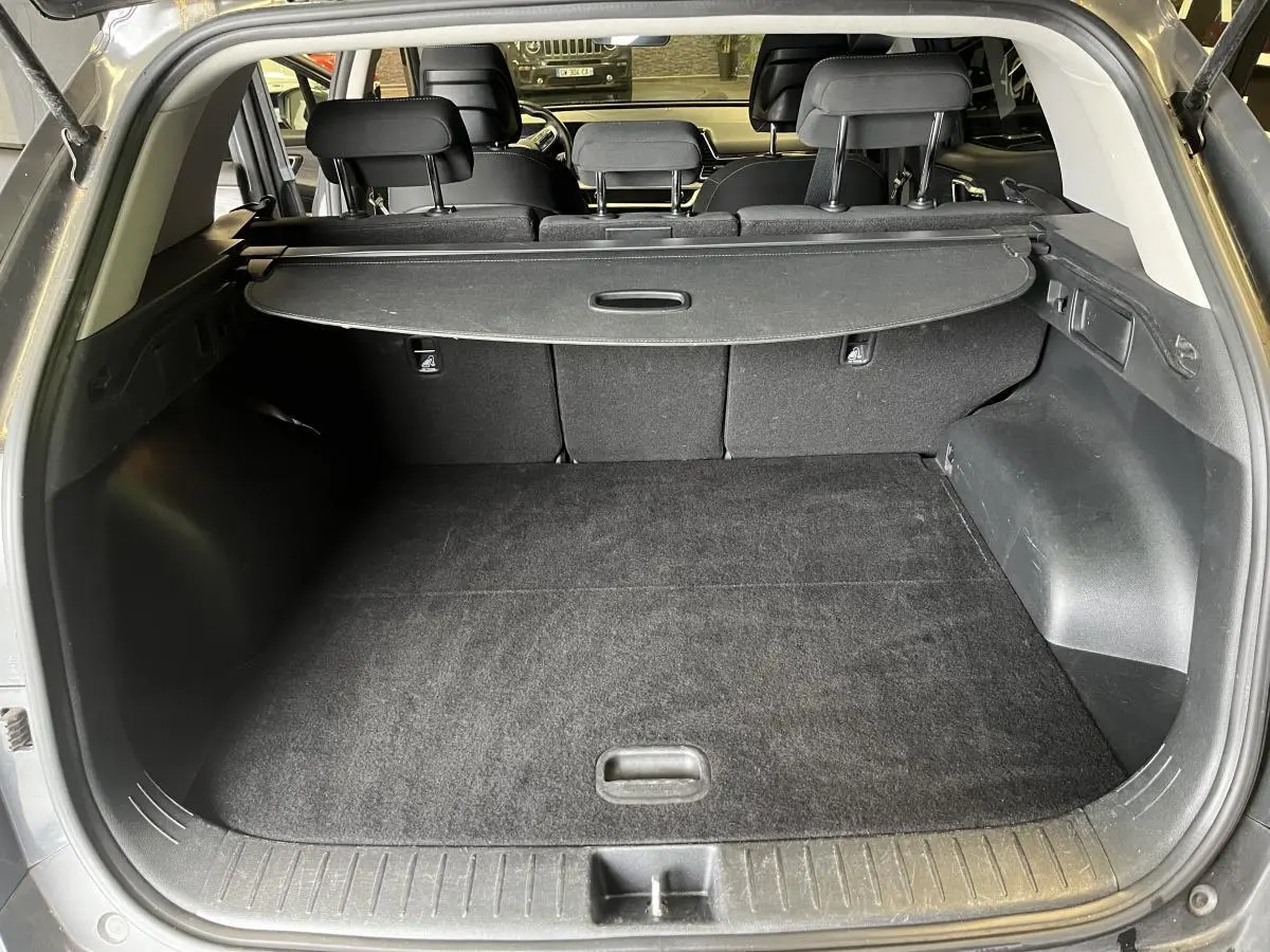 Coffre ouvert du Kia Sportage gris 2022, montrant le plancher plat et la plage arrière rétractable noire.