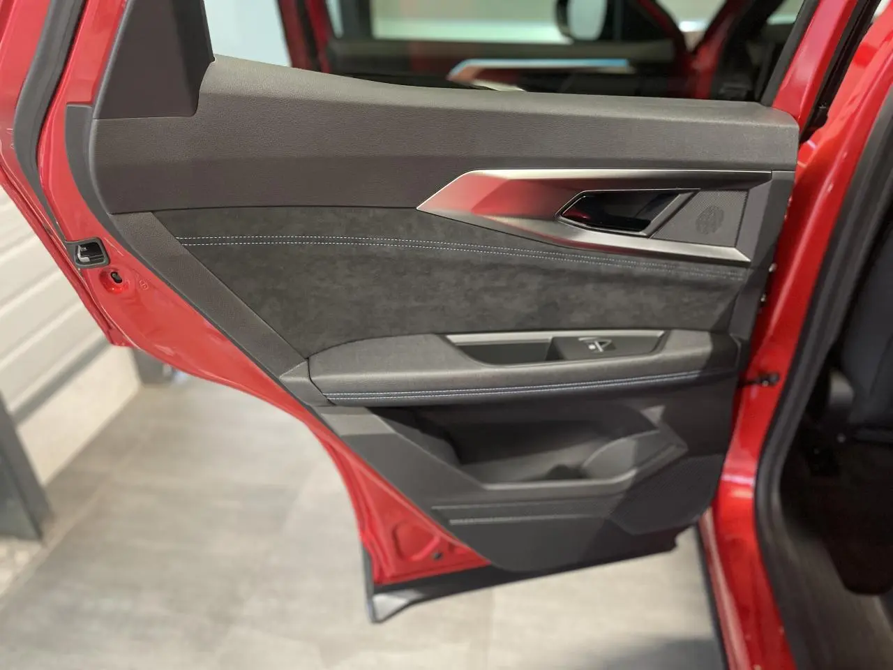 Vue rapprochée de la porte arrière gauche rouge métallisé du Renault Austral Esprit Alpine avec garniture noire et surpiqûres bleues.