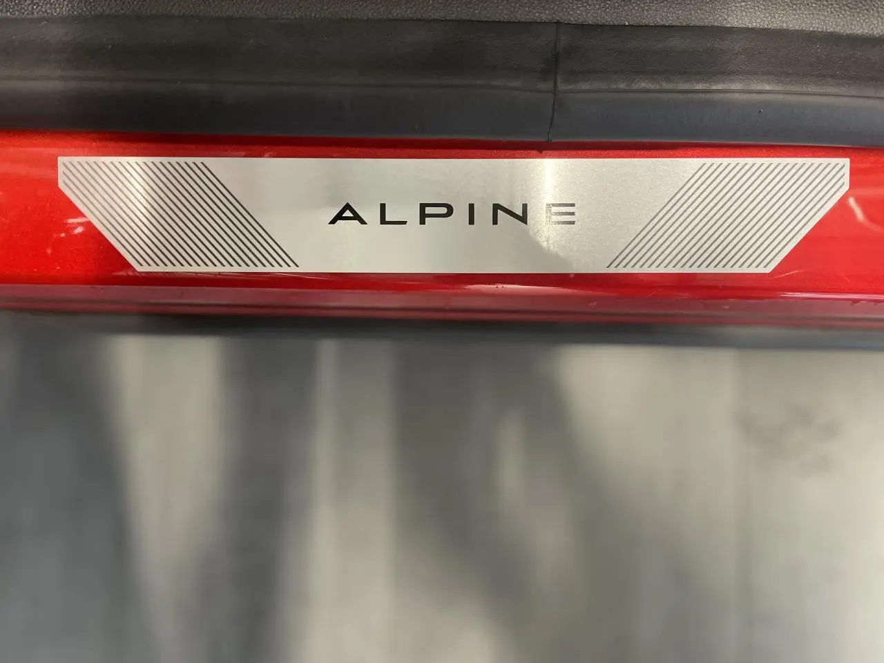 Plaque de seuil de porte ALPINE sur un Renault Austral rouge métallisé avec toit noir, vue en gros plan.