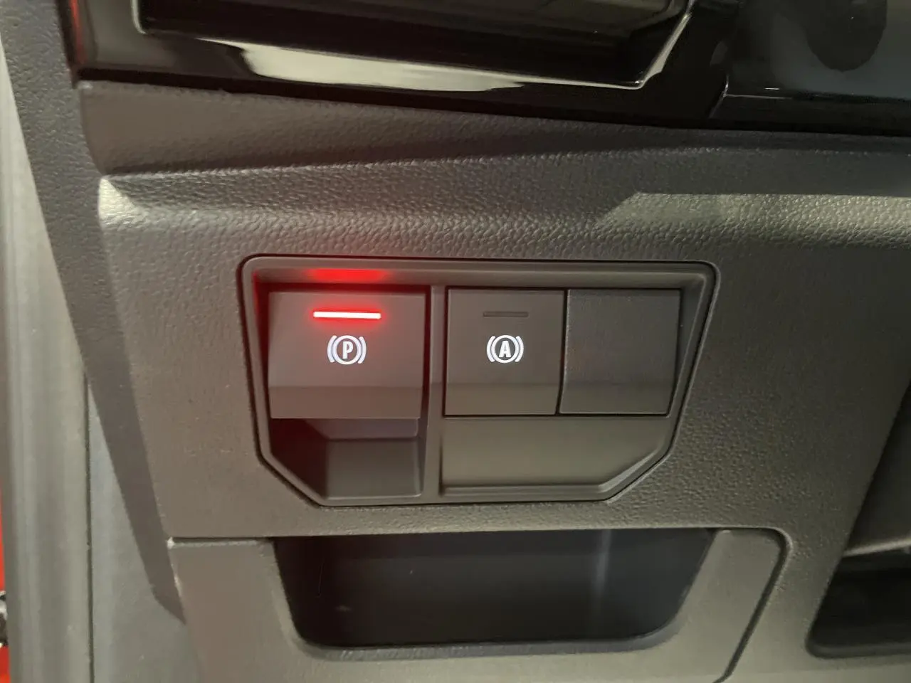 Gros plan sur les commandes du frein de parking électrique et du système start-stop du Renault Austral rouge métallisé.