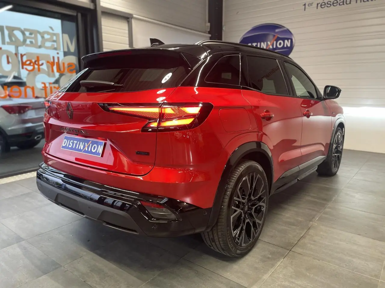 Vue 3/4 arrière droite du Renault Austral rouge métallisé avec toit noir et jantes alliage noires en showroom.