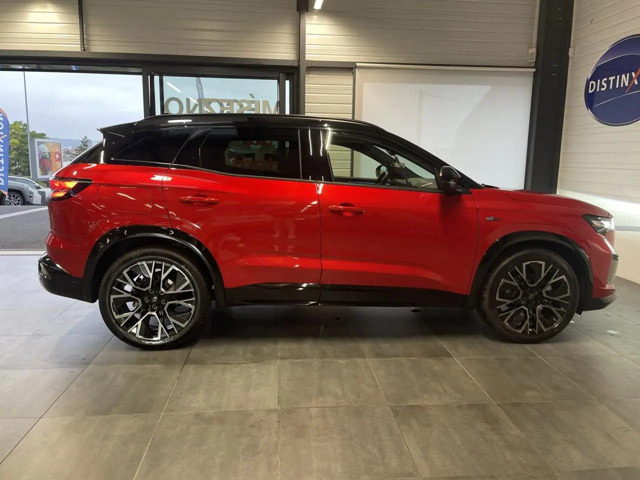 Profil droit du Renault Austral rouge métallisé avec toit noir et jantes alliage noires en showroom.