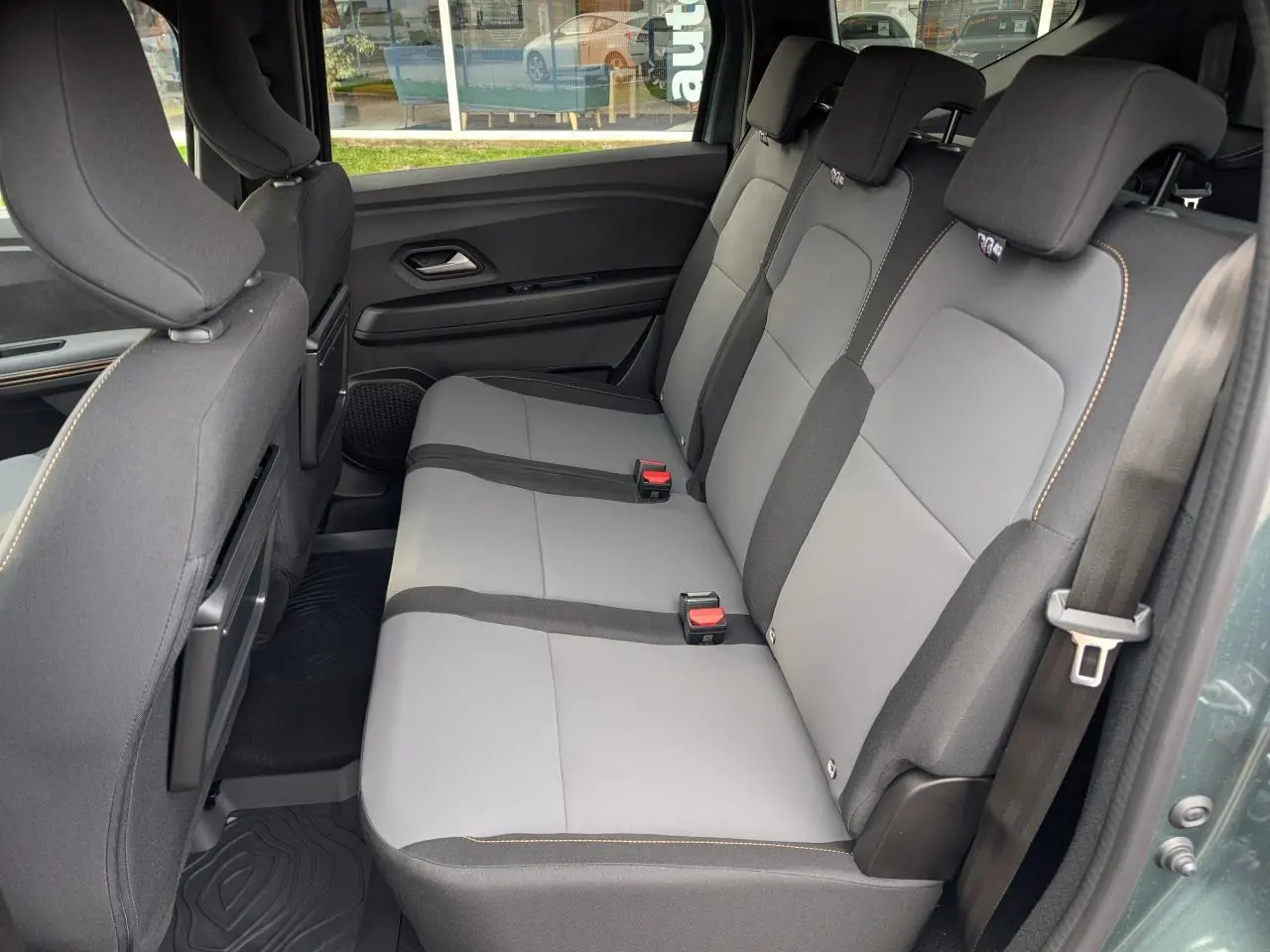 Vue latérale du siège arrière gris clair et noir du Dacia Jogger 2025 avec surpiqûres brun cuivré et tablettes aviation au dos des sièges avant.