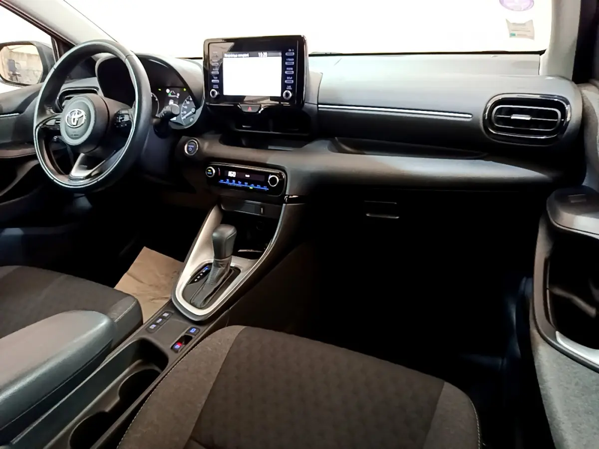 Intérieur avant droit de la Toyota Yaris Hybride 116h 2021, tableau de bord noir avec écran tactile central et volant cuir.