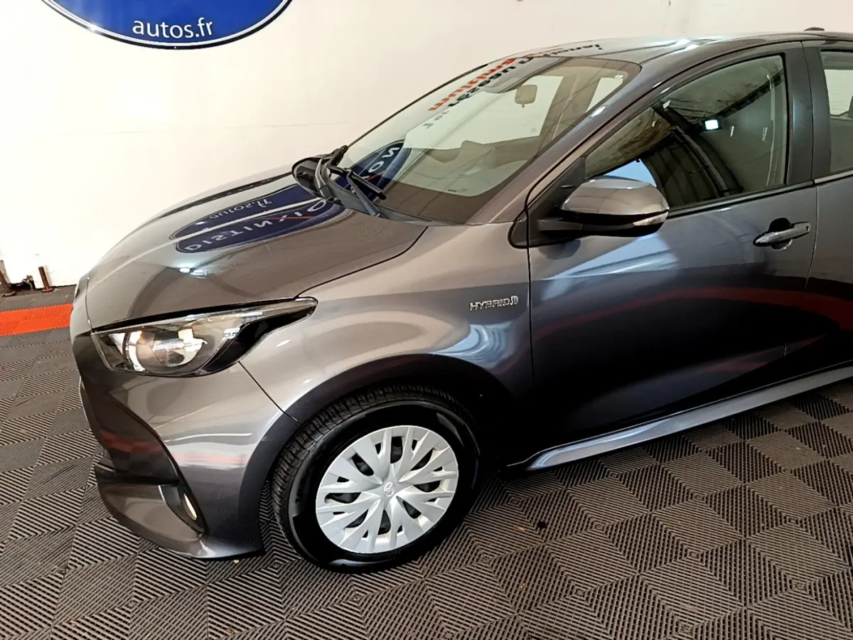 Vue 3/4 avant droit d'une Toyota Yaris hybride gris clair avec badge Hybrid visible sur l'aile avant.