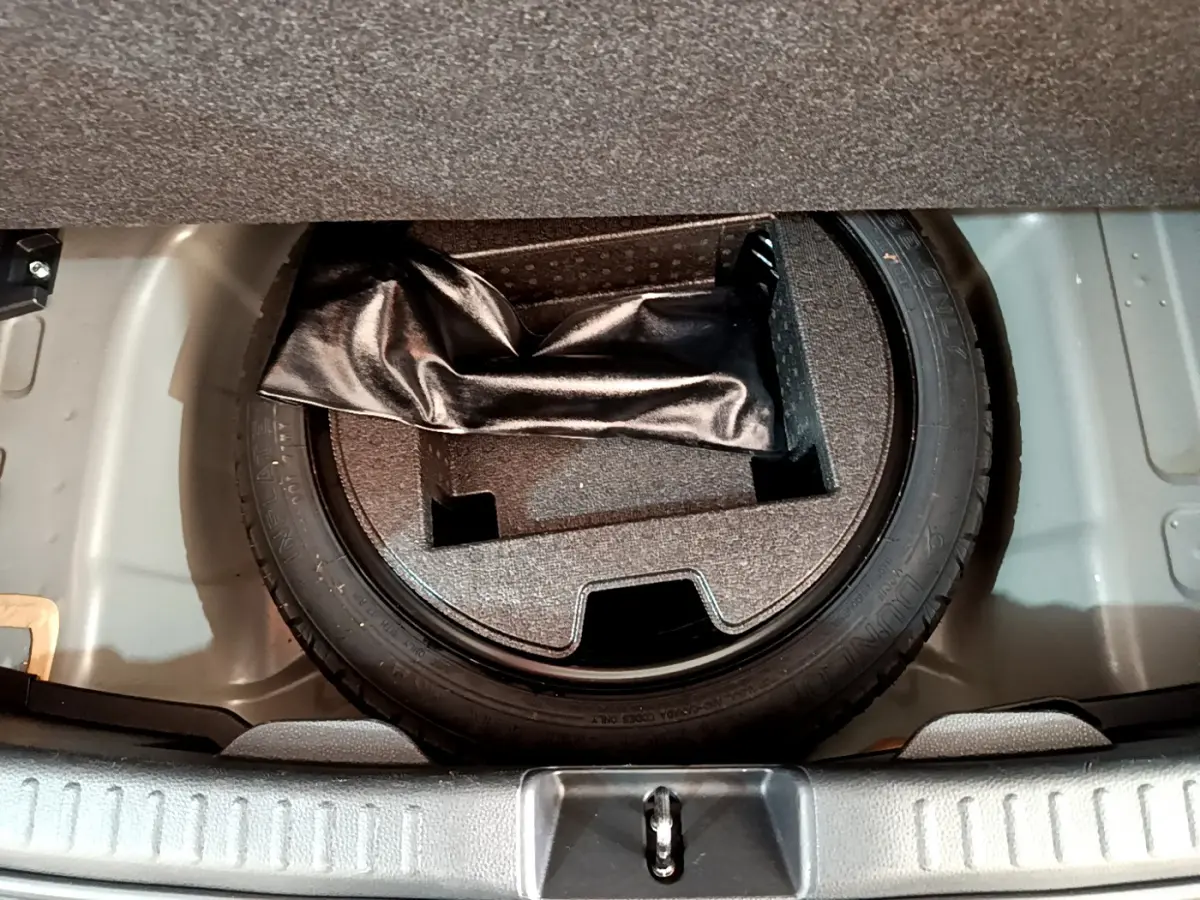 Pneu de secours et rangement sous le plancher du coffre d'une Toyota Yaris hybride gris clair, vue plongeante.